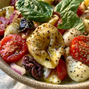 Macro photo of a single cheese tortellini coated in golden vinaigrette with cherry tomatoes. (Italian Tortellini Pasta Salad)