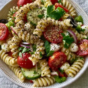 Close-up macro photo of glistening rotini pasta spirals coated in herb-flecked vinaigrette. (Pasta Salads)