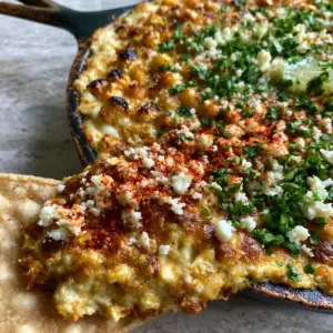 Split view showing overhead bubbly Baked Elote Dip and a close-up scoop with melted Monterey Jack cheese.