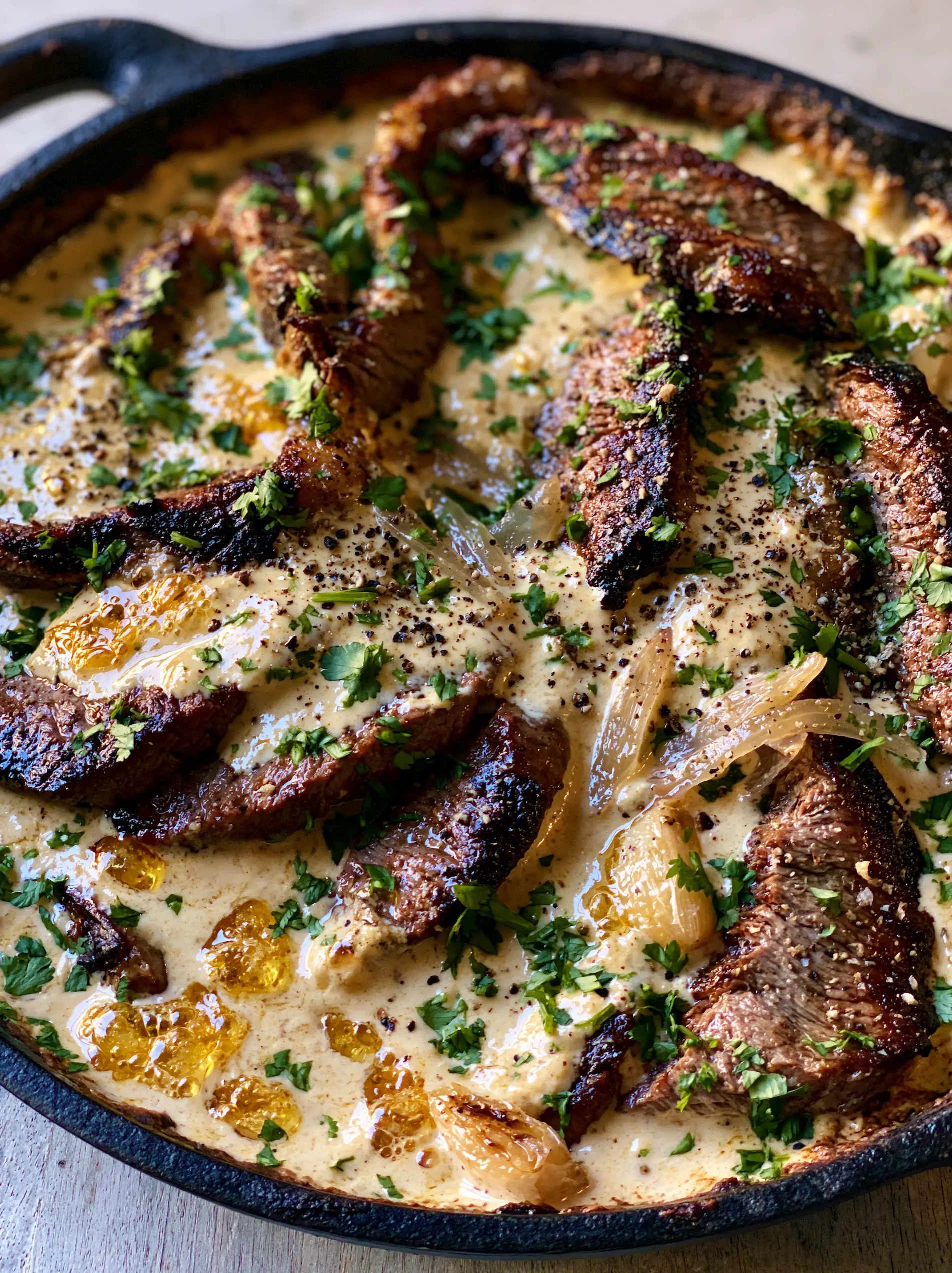 Bistec con Salsa Cremosa: The Ultimate Garlic Cream Steak in a Cast Iron Skillet 3 Top-down view of seared beef in a thick ivory sauce with whole roasted garlic cloves. (bistec con salsa cremosa)