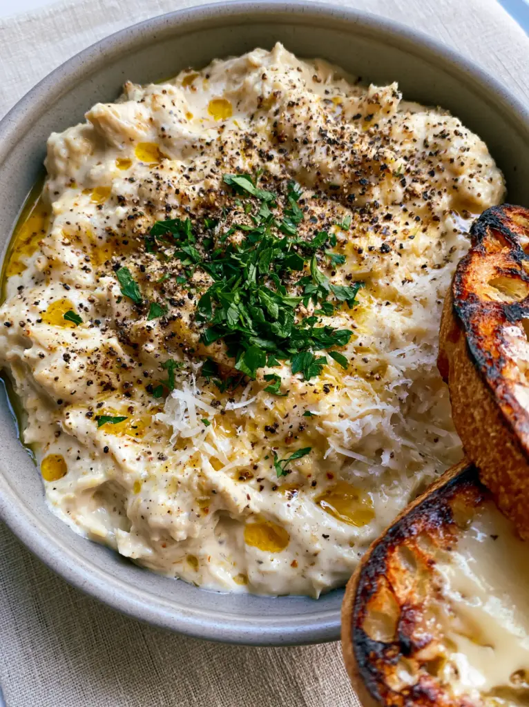 Crockpot Meals: The Ultimate Creamy Garlic Parmesan Shredded Chicken 1 Close-up of shredded chicken topped with coarse black pepper and fresh parsley garnish in a modern bowl.