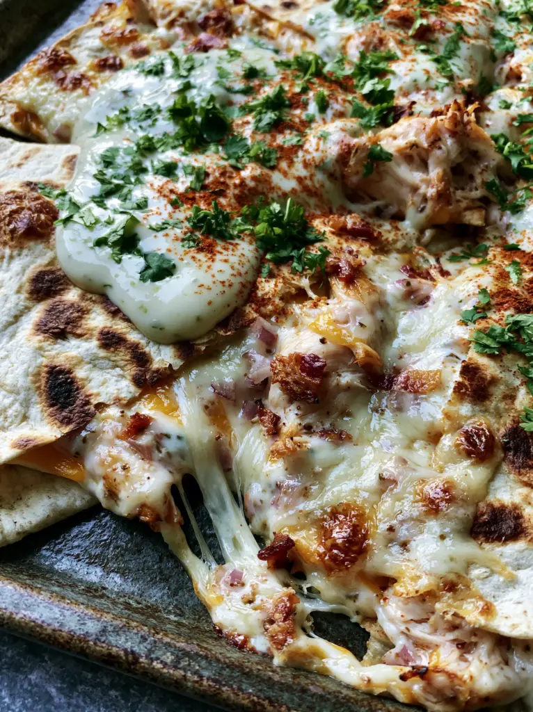 Back To School Dinner Ideas: Crispy Sheet-Pan Chicken Bacon Quesadillas 1 Top-down view of quesadilla triangles topped with thick lime crema, fresh cilantro, and a dusting of smoked paprika.