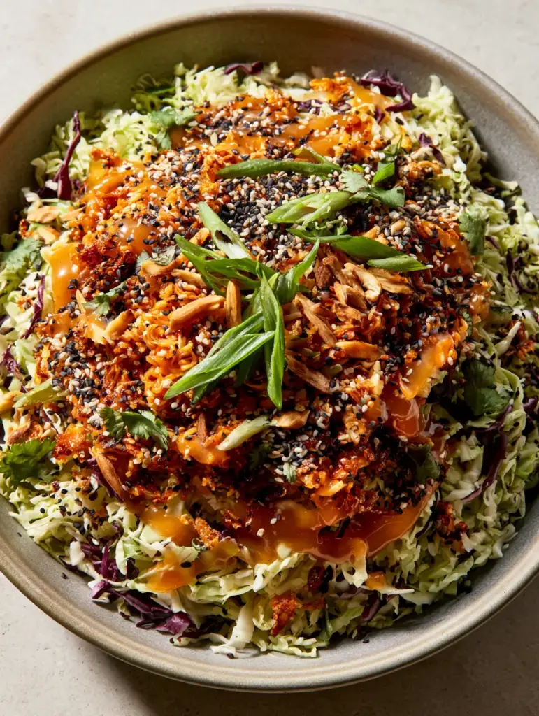 Close-up of glossy ginger sesame dressing drizzled over Napa cabbage salad with scallions and sesame seeds.