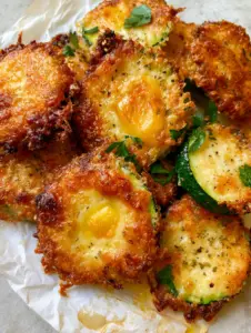 Extreme close-up of crispy parmesan zucchini rounds showing bubbly cheese texture and cracked black pepper specks.