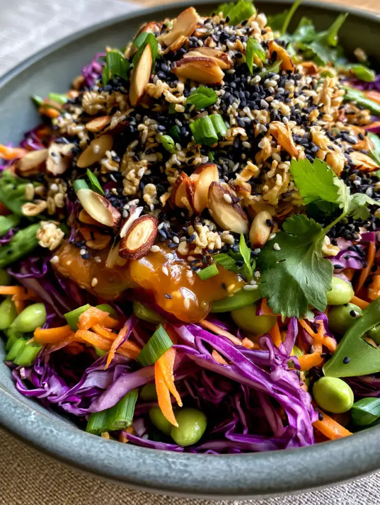 Close up of glossy amber sesame ginger dressing over fresh edamame and snap peas in a crunchy Asian salad.