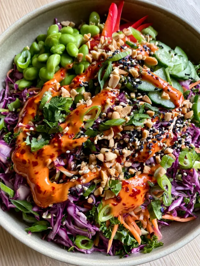 Spicy Asian Salad: The Ultimate Crunchy Chopped Salad with Chili Peanut Dressing 1 Close-up of a Spicy Asian Salad featuring thin strips of red bell pepper, green edamame, and toasted sesame seeds on a light wood background.
