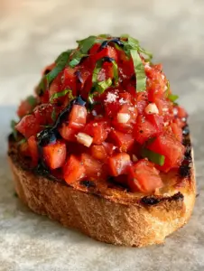 Macro photo of a single tomato bruschetta slice showing shatter-crisp texture and charred edges.