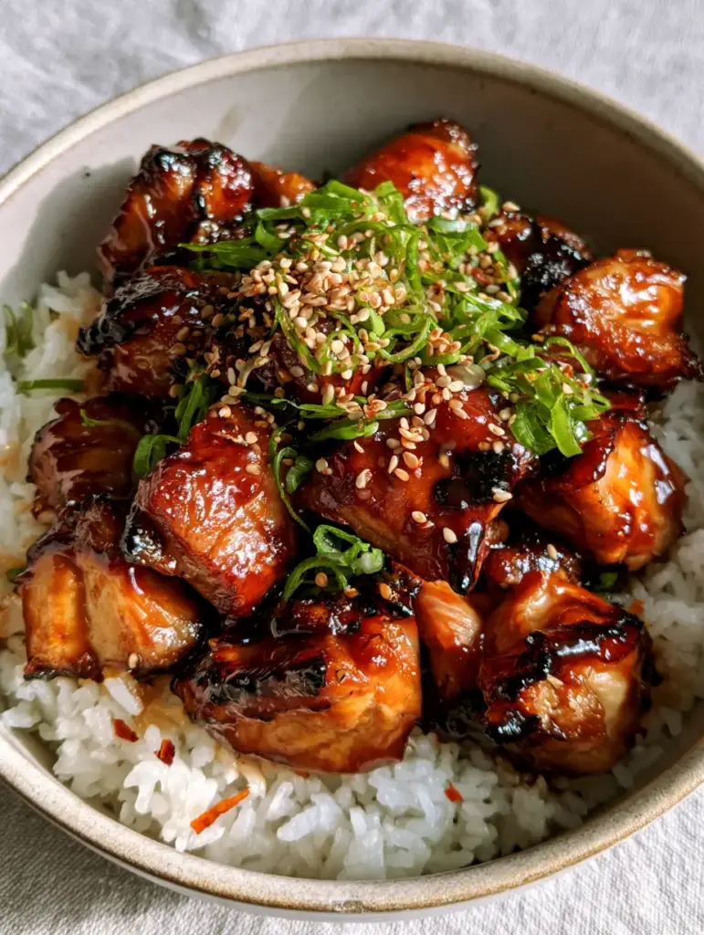 Teriyaki Chicken: Better-Than-Takeout Sticky Garlic Glaze 1 Stoneware bowl filled with steaming teriyaki chicken, topped with bright green scallions and sesame seeds against a light gray linen background.