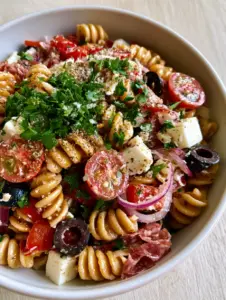 Close-up of glossy gluten-free rotini spirals coated in herb vinaigrette with visible cherry tomato seeds. (gluten-free Italian pasta salad)