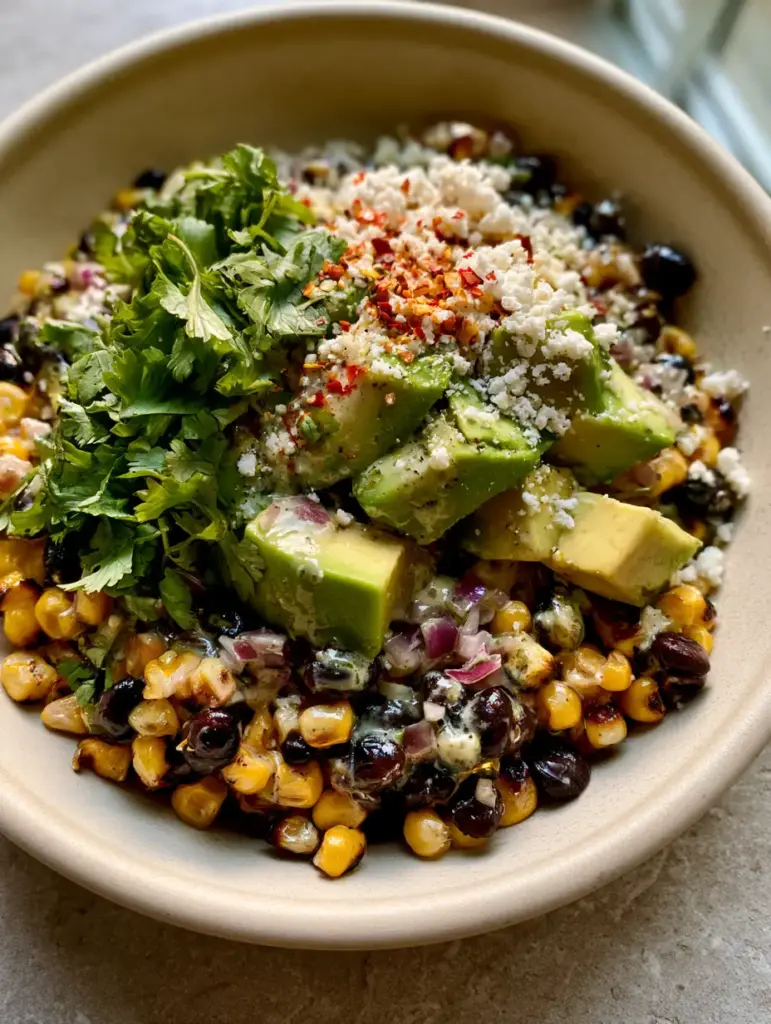 Corn Black Bean Avocado Salad with Fire-Charred Corn and Lime Crema 1 Close-up of lime-cilantro crema drizzled over a corn black bean avocado salad with crumbled cotija and chili flakes.