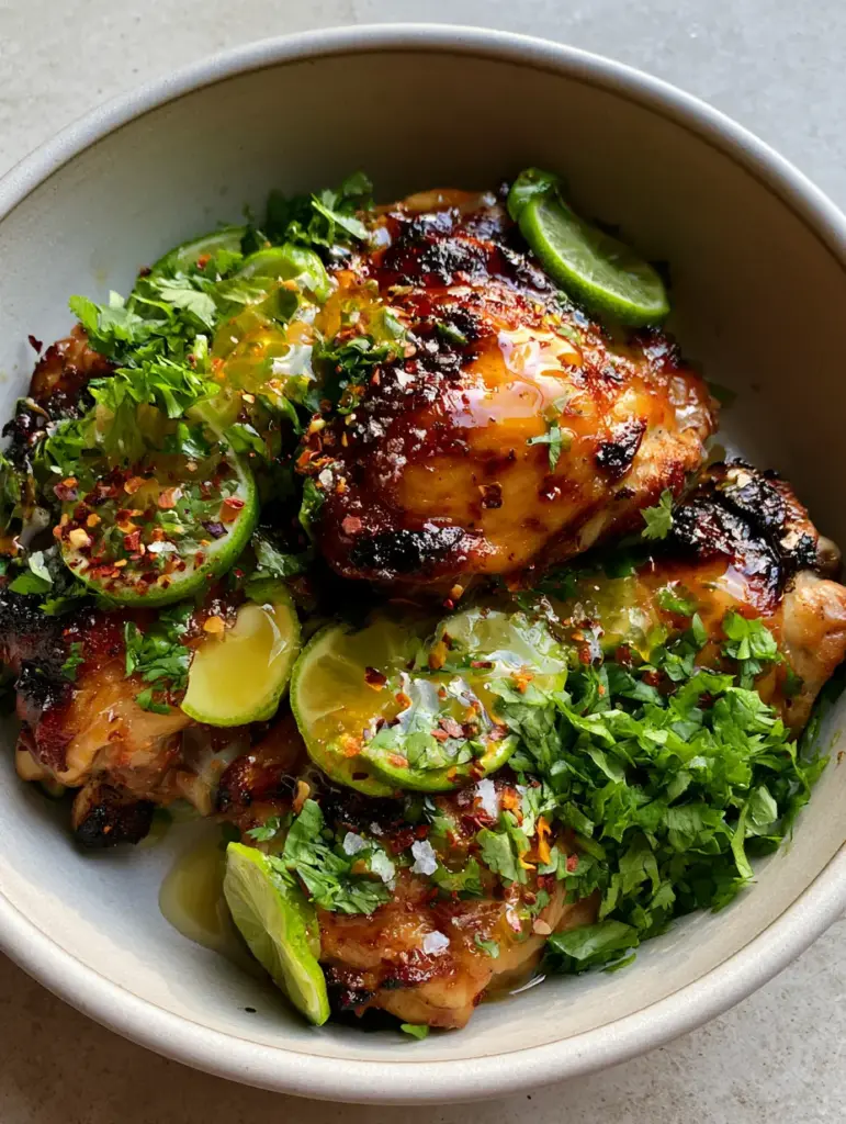 Succulent grilled chicken thighs in a ceramic dish with cilantro and lime juice droplets.