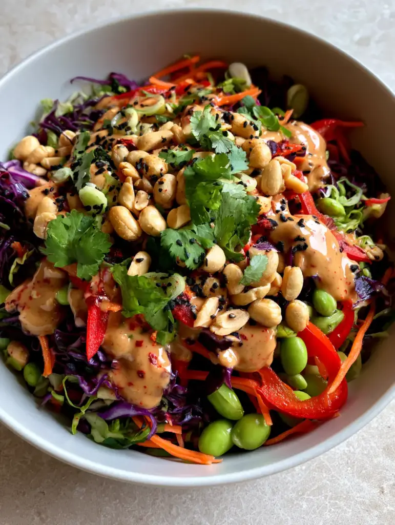 A heavy drizzle of light brown peanut sauce over a bed of purple cabbage and green edamame.